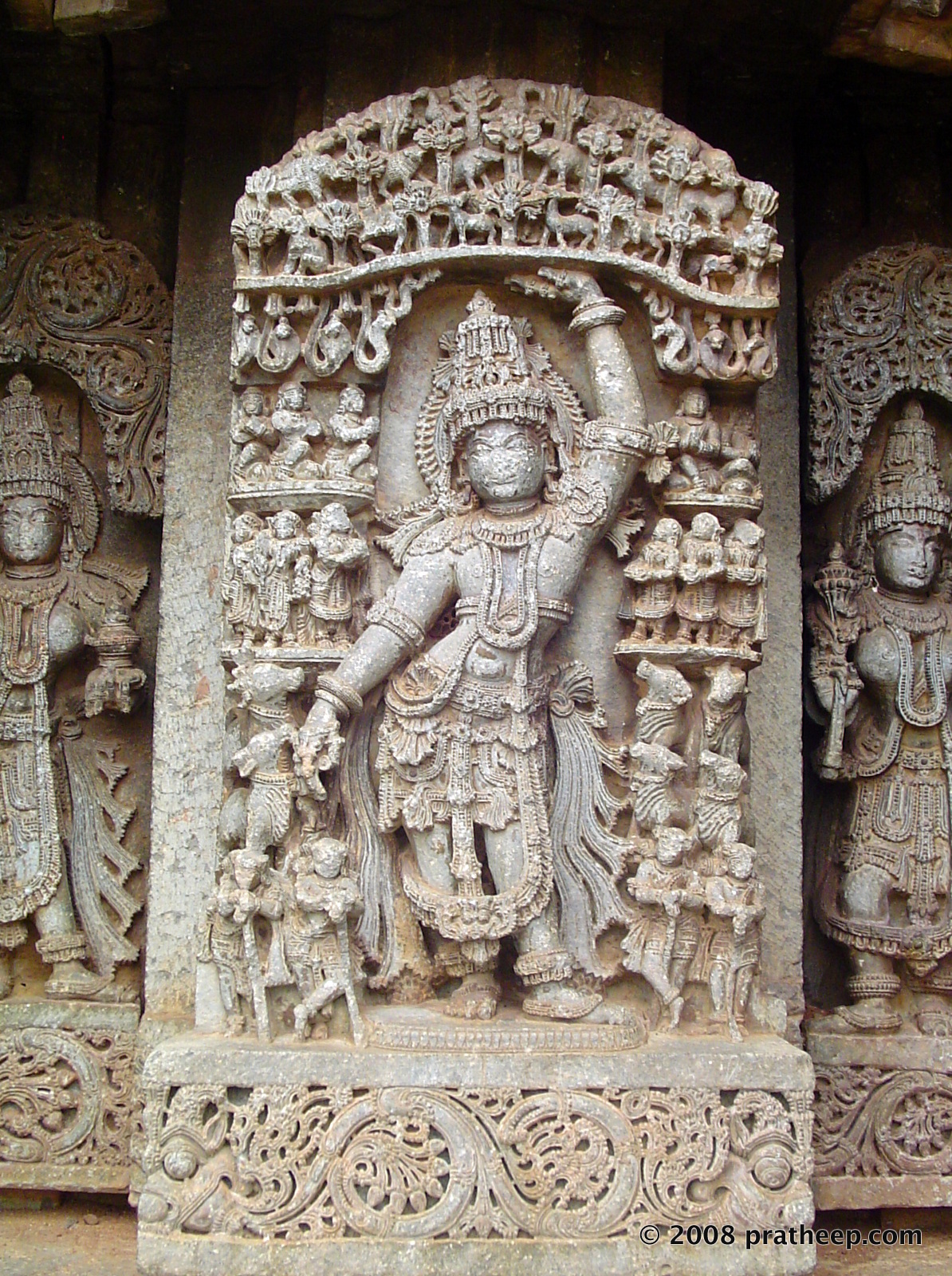 Krishna lifting Govardhana hill, use it as an umbrella to protect the inhabitant from the deluge. Note the calf licking his right hand! Image on the outer wall of the Hosaholalu temple. 
